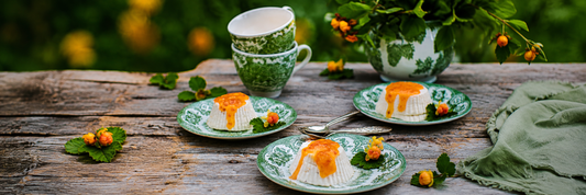 Skandinavisches Dessert mit Moltebeeren und Moltebeerensoße auf grün-weißem Porzellan auf einem rustikalen Holztisch.