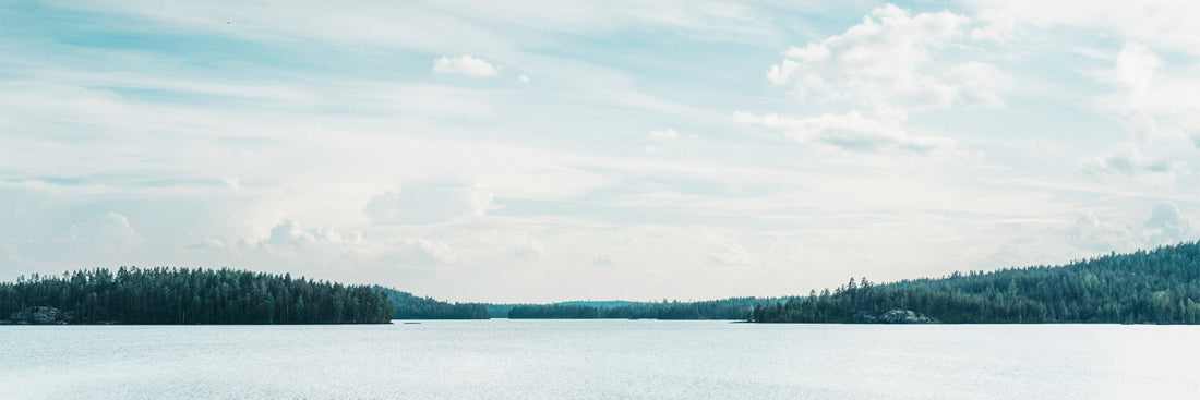 Ruhiger finnischer See mit spiegelglatter Wasseroberfläche und dichtem Kiefernwald am Horizont