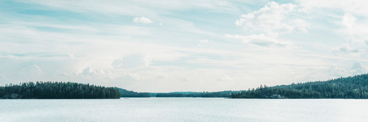 Ruhiger finnischer See mit spiegelglatter Wasseroberfläche und dichtem Kiefernwald am Horizont