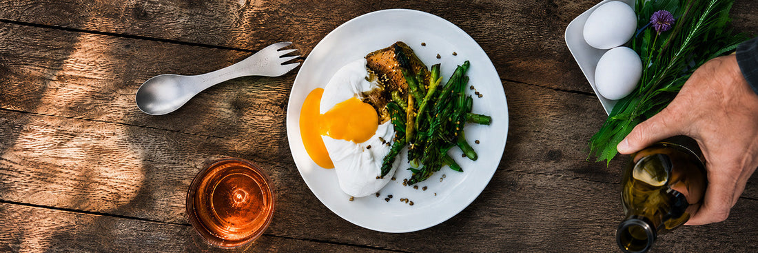 Gegrillter grüner Spargel mit Burrata, Eigelb und Honig-Zitronen-Soße, angerichtet auf einem Teller, garniert mit Bärlauch und geröstetem Buchweizen