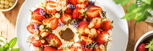 Schwedische Erdbeertorte Jordgubbstårta von oben – mit frischen halbierten Erdbeeren, weißen Johannisbeeren und essbaren Blüten dekoriert – Mittsommer-Rezept aus „Meine schwedische Backstube" von Moritz Reuter.