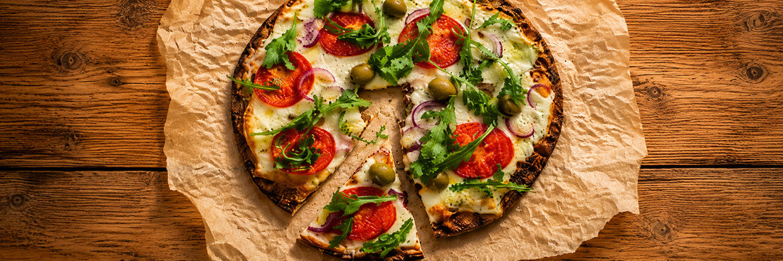 Frisch belegte Knackebrot Pizza mit Tomaten, Rucola, grünen Oliven und roten Zwiebeln auf Backpapier auf einem rustikalen Holztisch.