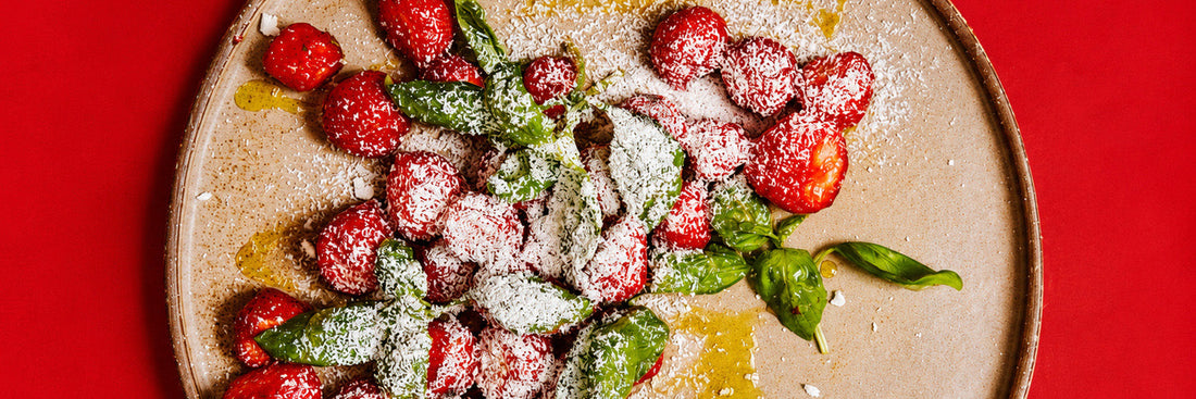 Marinierte Erdbeeren mit frischem Basilikum auf einem Teller, daneben eine Reibe mit gefrorenem Feta – Rezept aus „Das Schweden-Kochbuch" von Niklas Ekstedt
