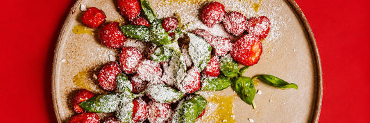 Marinierte Erdbeeren mit frischem Basilikum auf einem Teller, daneben eine Reibe mit gefrorenem Feta – Rezept aus „Das Schweden-Kochbuch" von Niklas Ekstedt