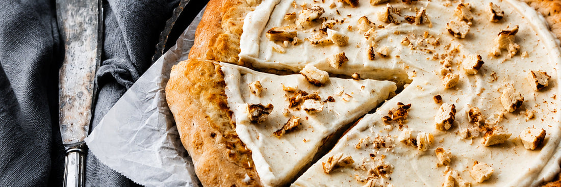 Zimtschnecken-Pizza mit cremigem Zimt-Frischkäse-Belag und knusprigem Rand, angeschnitten auf Backpapier serviert.
