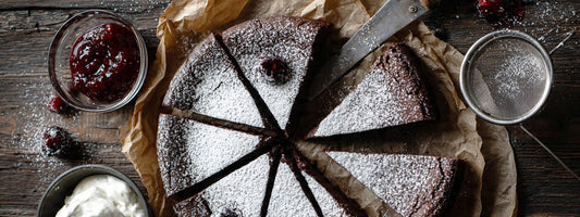 Schwedischer Schokoladenkuchen Kladdkaka mit Puderzucker, Sahne und Beerenkonfitüre
