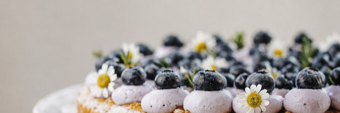Schwedische Blåbärstårta mit Heidelbeeren, Mascarponecreme und kleinen Blüten auf einer weißen Tortenplatte.