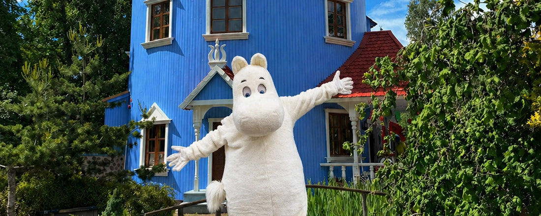 Weiße Mumin-Figur vor blauem Holzhaus in grüner Umgebung