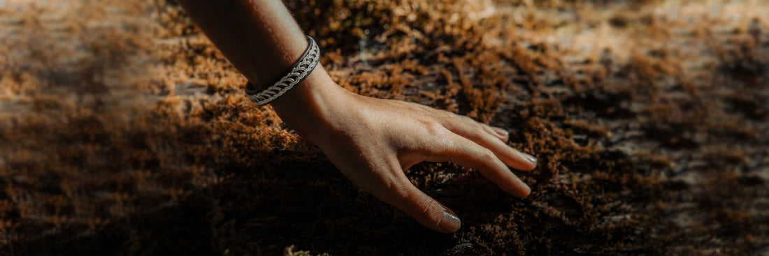 Silbernes Sámi-Armband am Handgelenk vor moosbewachsener Baumrinde