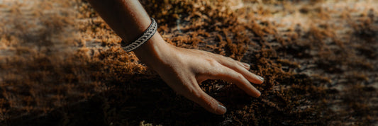 Silbernes Sámi-Armband am Handgelenk vor moosbewachsener Baumrinde